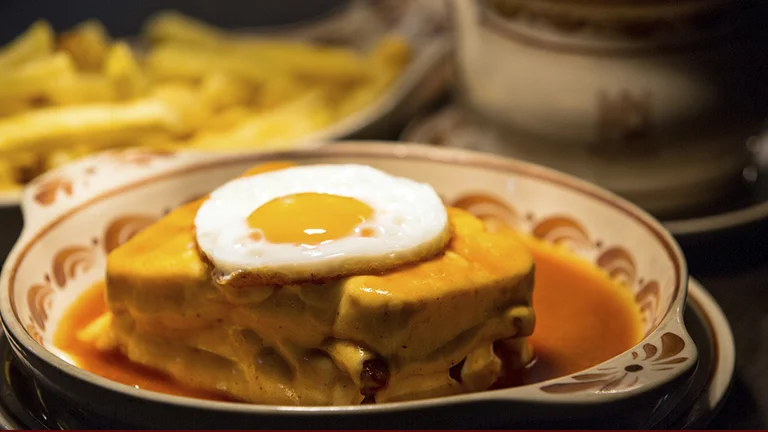 Sandwich topped with a fried egg in orange sauce, with fries in the background.