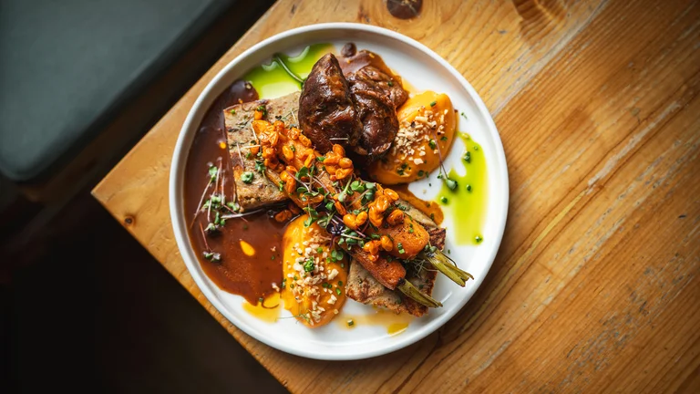 Gourmet dish with meat, vegetables, and colorful sauces on a white plate.