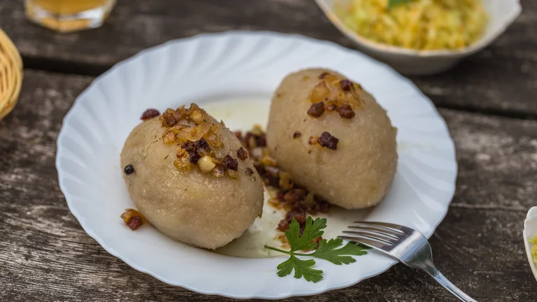 Two potato dumplings topped with fried onions on a white plate with parsley garnish.