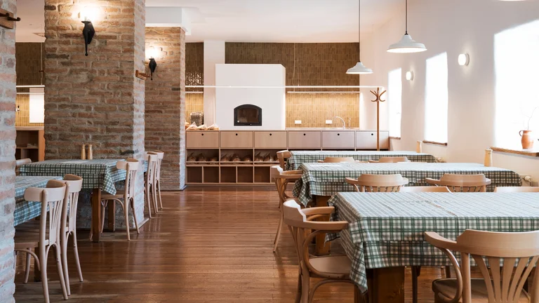 Empty restaurant dining area with wooden tables and green plaid tablecloths.