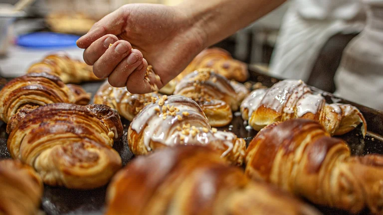 Hand sprinkling nuts on freshly baked croissants with icing.