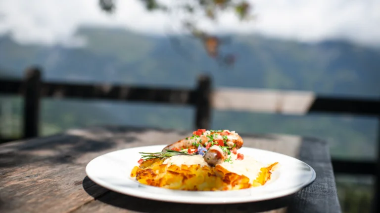 Grilled chicken with vegetables on mashed potatoes, served outdoors with mountains in background.