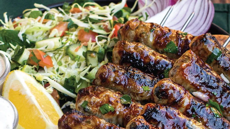 Grilled meat skewers with salad, sliced onion, sauces, and a lemon wedge on a plate.