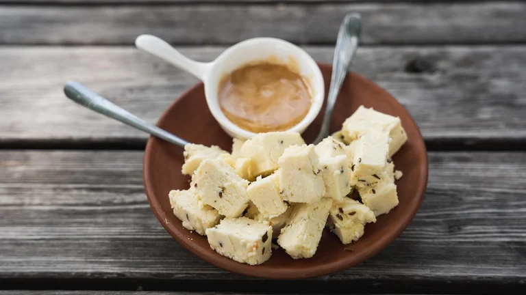 Plate of white fudge pieces with a small bowl of caramel dip on a wooden table.