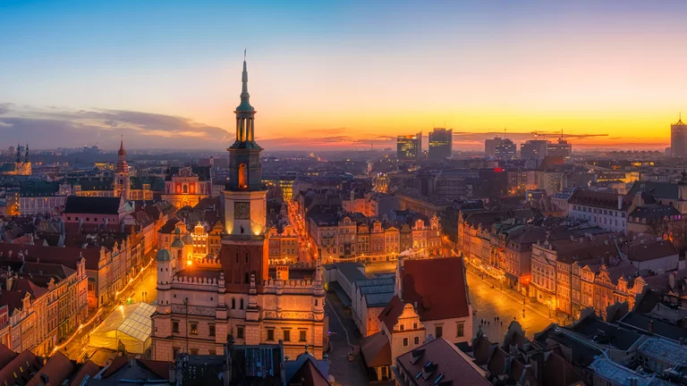 Cityscape at sunset with illuminated buildings and a central tower.