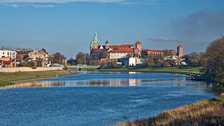 Castle on a hill beside a river under a clear blue sky.