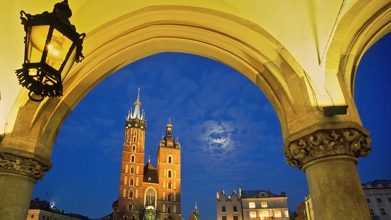 Gothic cathedral towers framed by arch at dusk, with moon and lantern above.
