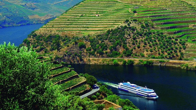 A river cruise ship sails between green terraced hills under a clear sky.