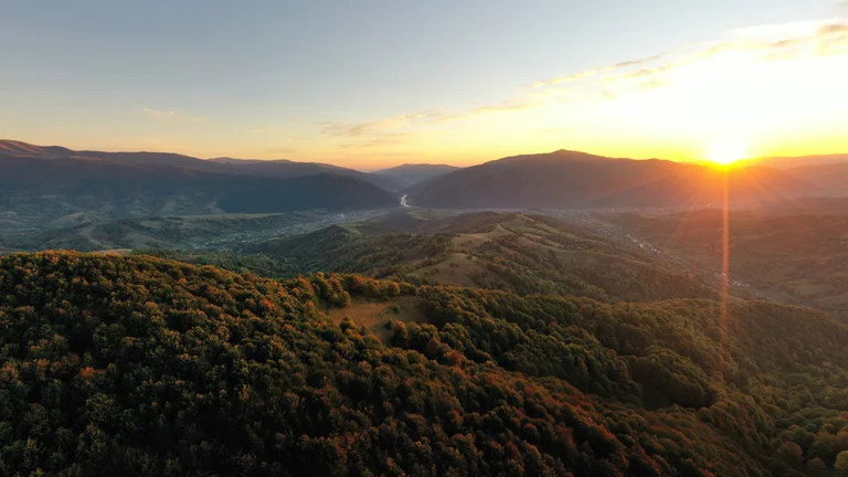 Sunrise over forested mountains with a river winding through the valley.