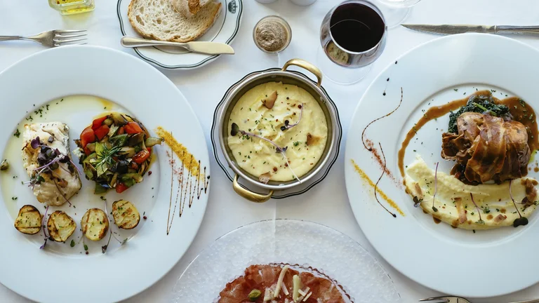 Elegant table setting with gourmet plated dishes, wine, bread, and a creamy dip in the center.