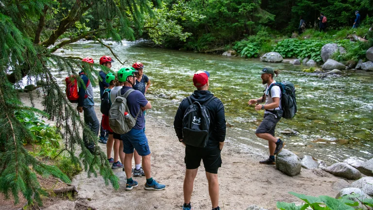 Group of hikers listening to a guide by a forest river.