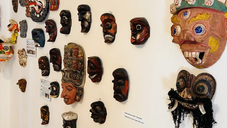 Colorful traditional masks displayed on a white wall in a museum or gallery.