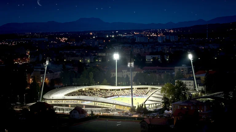 Stadium illuminated at night with a cityscape and mountains in the background.