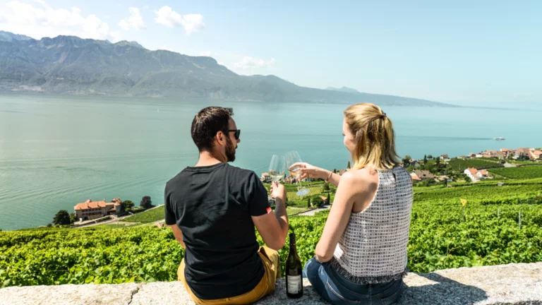 Couple enjoying wine overlooking a lake and vineyards with mountains in the background.