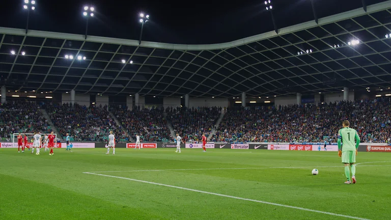 Goalkeeper in green preparing for a kick during a night soccer match in a crowded stadium.