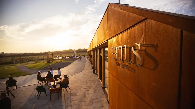 People sitting at outdoor tables near a modern building at sunset.