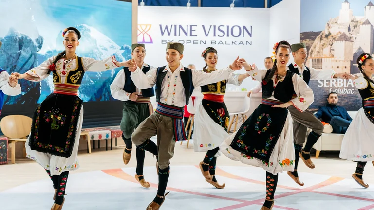 Dancers in traditional Balkan costumes performing a folk dance indoors.