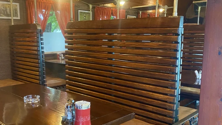 Wooden booths in a warmly lit restaurant with red curtains and condiments on the table.