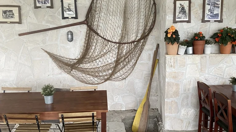 Cozy patio with tables, chairs, nautical decor, hanging net, and potted flowers on a stone wall.