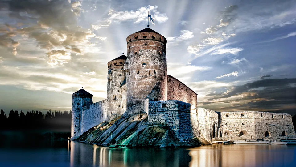 Stone castle with towers reflected in calm water, dramatic sun rays in the sky.