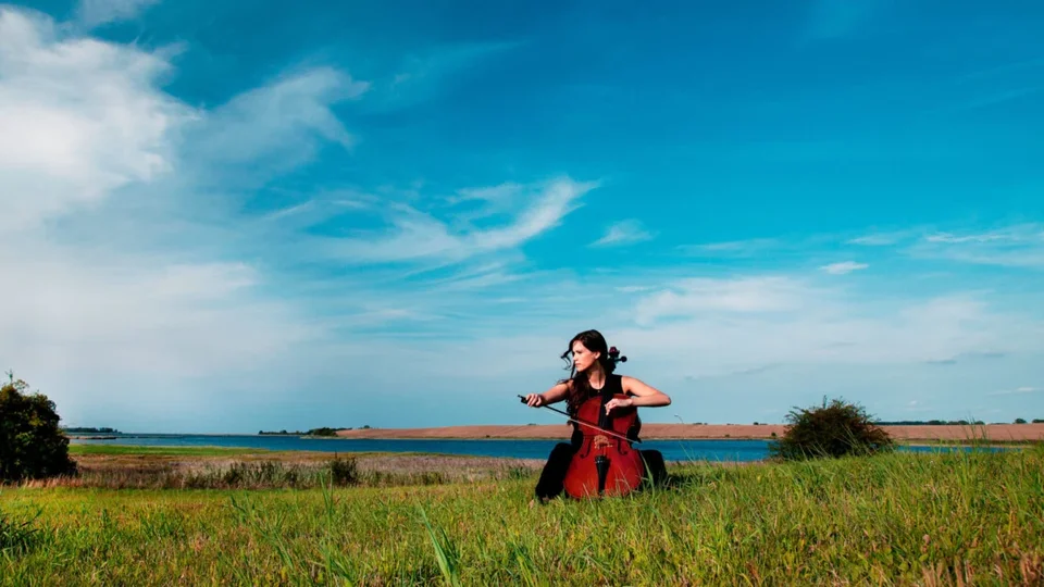 Woman in a red dress running through a grassy field under a bright blue sky.