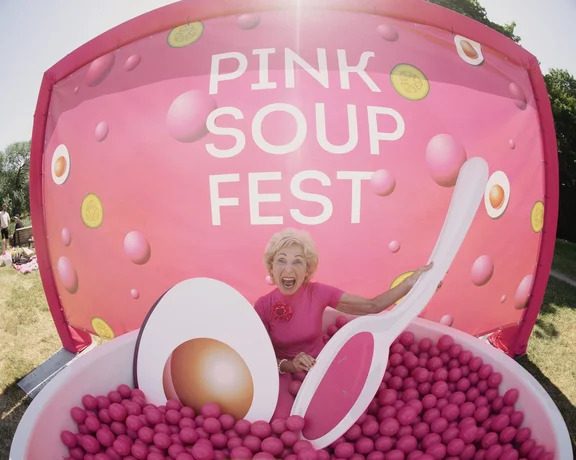 A person inside of a pool filled with pink balls with a background stating Pink soup fest in Vilnius.
