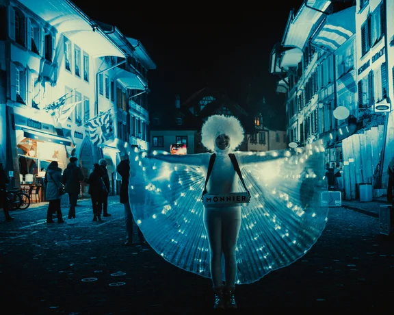 A woman in a light-up costume on a cobblestone street at night, with illuminated buildings in the background.
