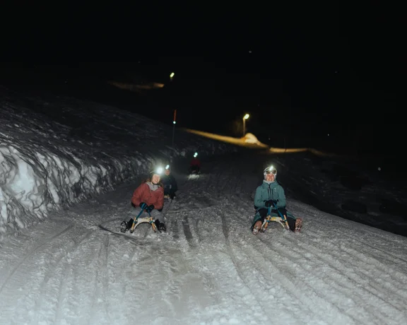 People sliding through a ski slope on a sleigh during the night.