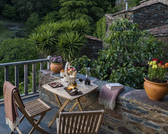 Rustic balcony with a table set for two, overlooking lush greenery.