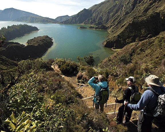 Hikers observing the scenic mountainous Fogo lake in the Azores, Portugal, on a sunny day.