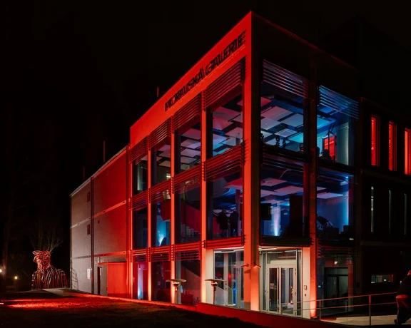 Moravian gallery in Brno illuminated in red at night with a sculpture outside.