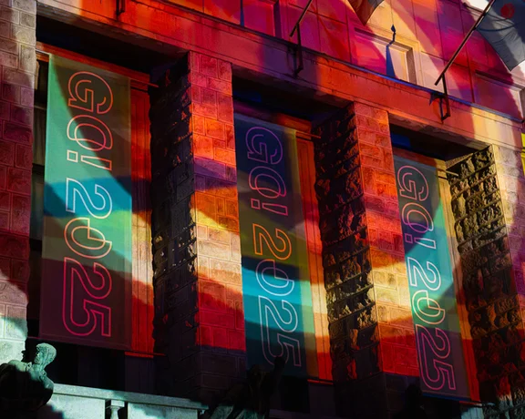 A building facade illuminated with colorful light projections reading "GQ 2025".