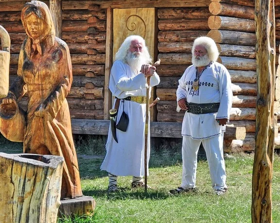 Wooden sculptures and people in traditional clothing by a log cabin at the Sculpture Camp in Polovragi Village.