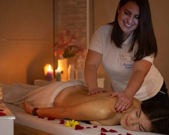 A woman receiving a back massage in a candlelit room with flower petals scattered around in a spa in Serbia.