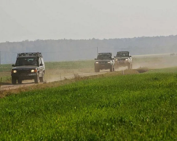Three SUVs driving on a dusty rural road beside a green field.
