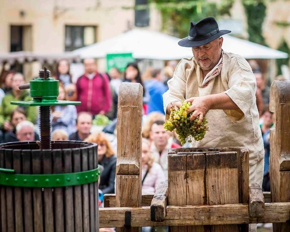 A person operating a traditional wine press at a crowded at the Modran vintage.event.