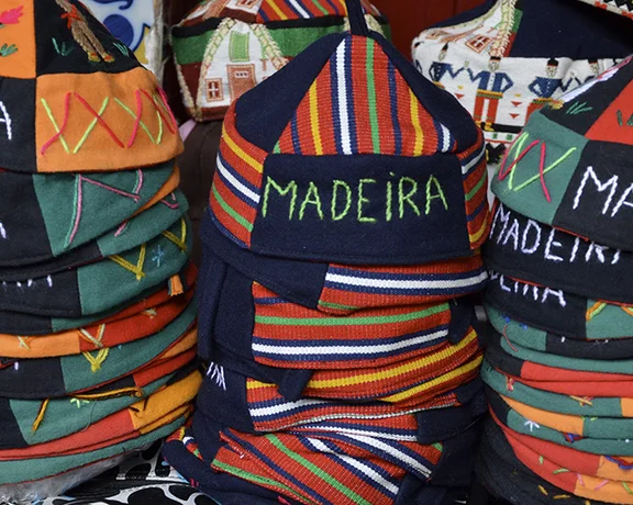 Colorful stacks of traditional Madeira hats, featuring embroidered "MADEIRA" WORD and vibrant patterns, displayed together.