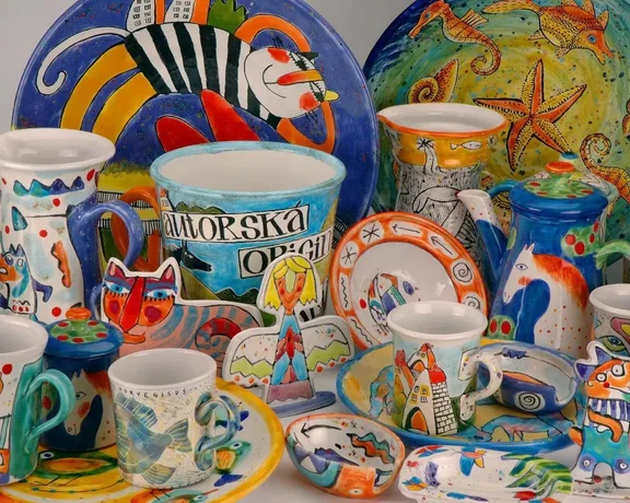 A colorful collection of hand-painted pottery, including plates, mugs, and jugs featuring whimsical animal and nature designs.