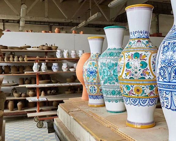 A pottery workshop displays intricately painted vases and various pottery items on wooden shelves under natural light.