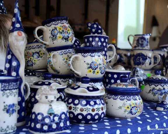 A display of intricately patterned Polish pottery in blue and white, featuring mugs, jugs, and decorative figurines.