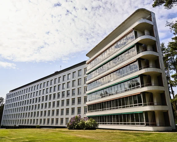 Iconic white building with large windows and rounded balconies, surrounded by lush greenery.