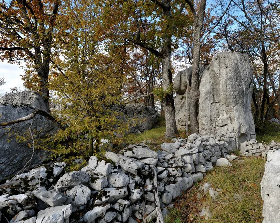 Scenic landscape featuring large limestone rocks surrounded by autumn foliage and a weathered stone wall under a bright blue sky.