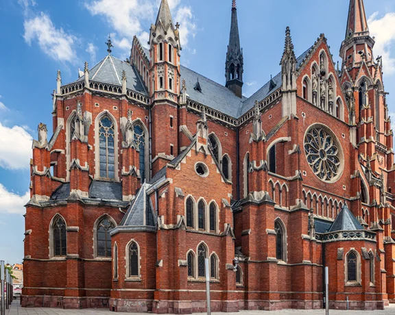A striking Gothic-style church with red brick façade, intricate details, and tall spires against a clear blue sky.