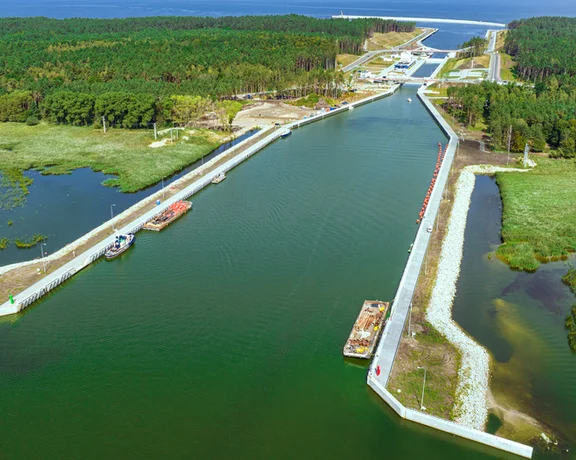 Aerial view of a river channel surrounded by lush forests, leading to a marina with boats along the banks and a launching ramp.