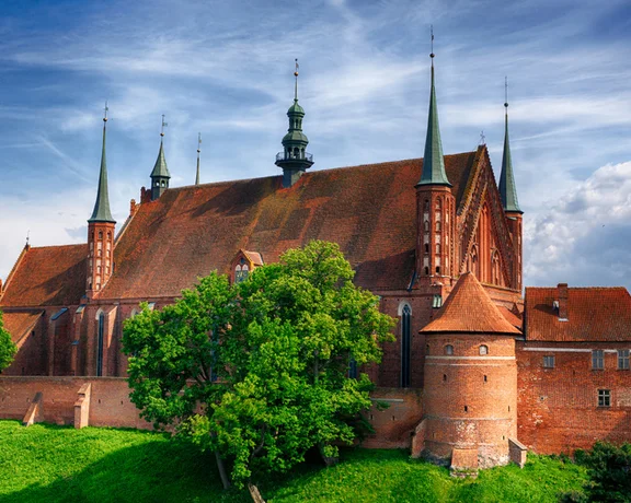 Frombork Cathedral in Poland surrounded by greenery under a vibrant sky.