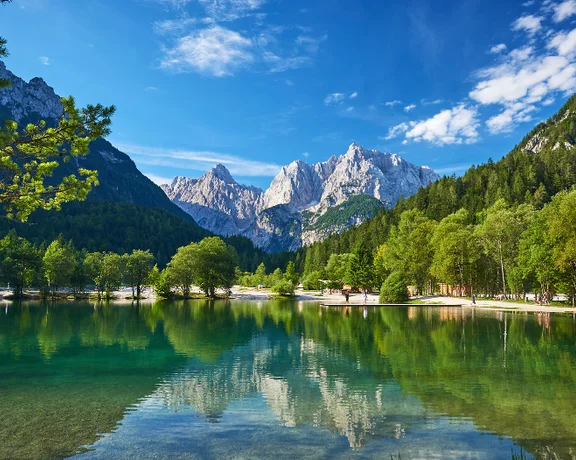 Stunning view of Lake Jasna in Slovenia, with turquoise waters, alpine peaks, and lush forests.