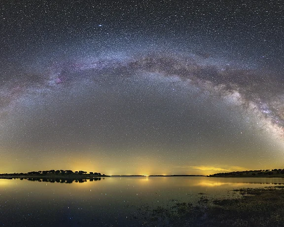 Milky Way arch reflected over Alqueva Lake at night.