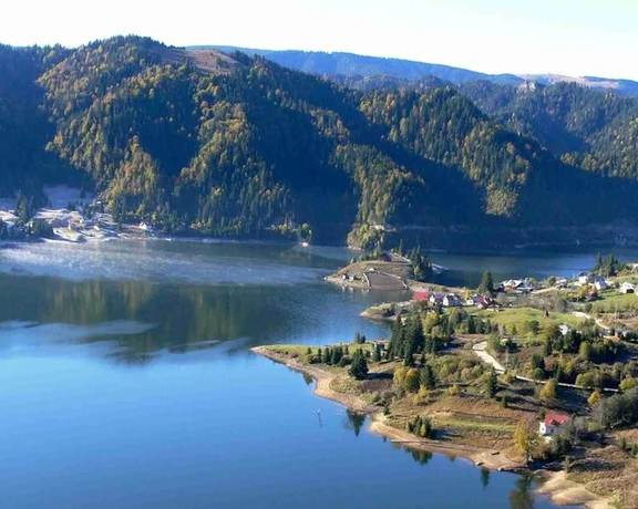 Colibita Lake surrounded by mountains and forests in autumn.