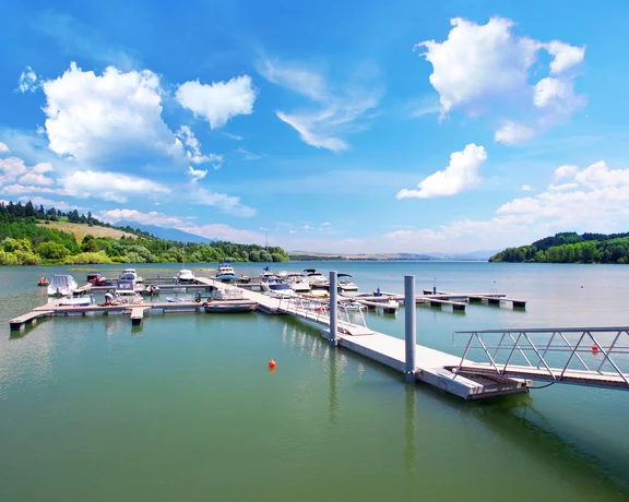 Boats docked at a marina on Oravská Reservoir under a bright sky.