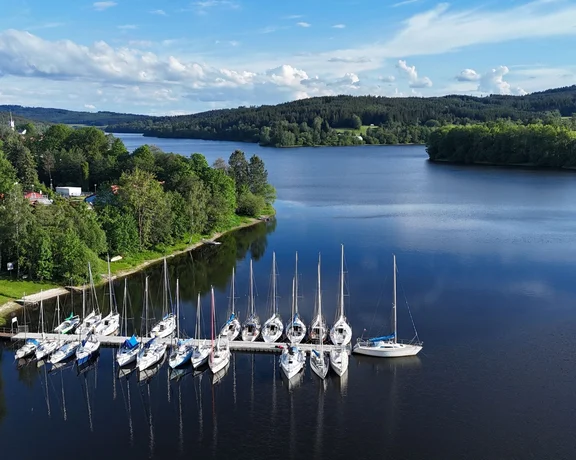 Sailboats moored on calm waters with a forested landscape.